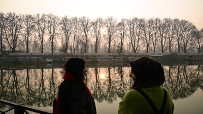 Two women talking by the river at sunset, reflecting on Kashmiri Pandit issues.