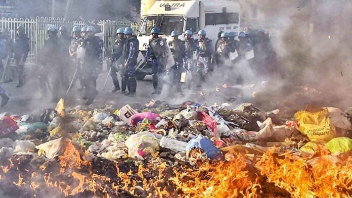 Clash between protesters and police at garbage dump with fire and smoke.