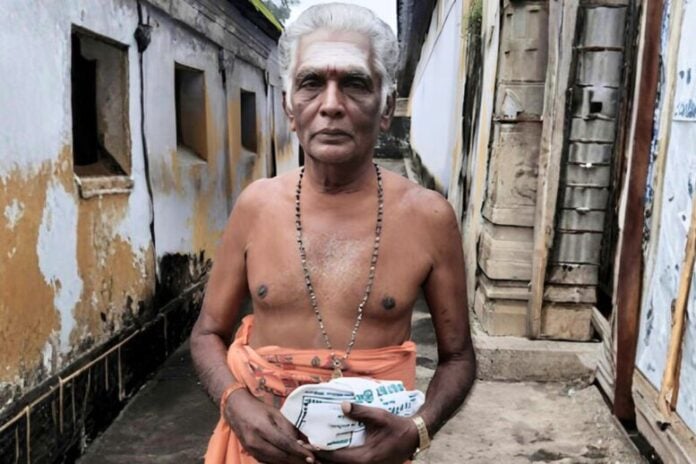 Elderly Saivite priest holding prayer book, reflecting sacred tradition and spiritual voice.