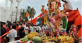 Celebration of Ganesh Chaturthi with large idol, flowers, and devotees.