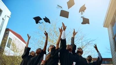 Group of diverse students celebrating graduation outdoors, tossing caps in the air.