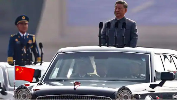 Chinese President Xi Jinping during a military parade with officials and a Chinese flag.
