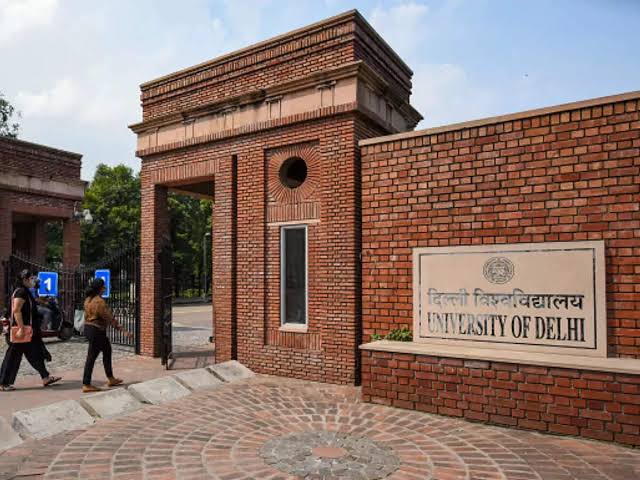 Entrance to University of Delhi with students walking past brick gate.