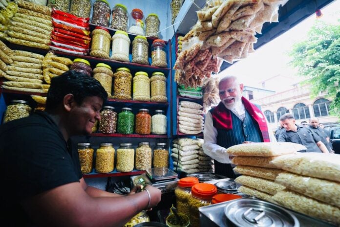 Jhalmuri seller selling snacks at a busy market stall, with jars of ingredients and customers.