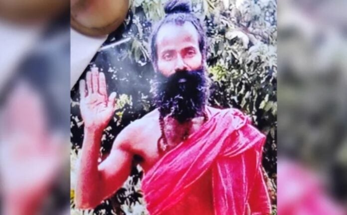 Hindu sadhu with long beard and traditional attire, raising hand in blessing, outdoors.