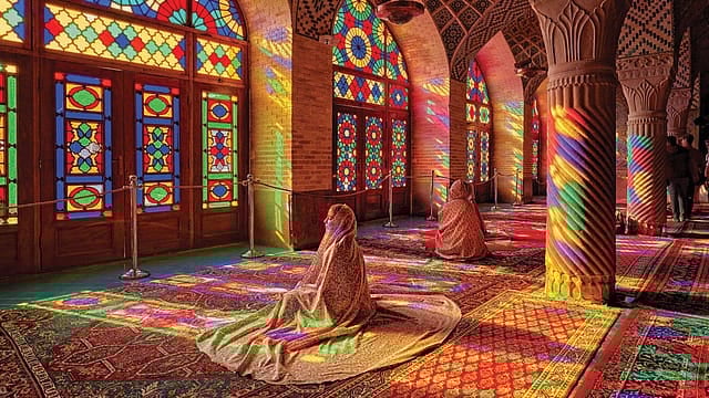 Intricate stained glass windows casting colorful light inside a mosque.