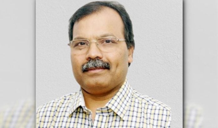 Close-up of an Indian scholar with glasses and mustache, wearing a checkered shirt.