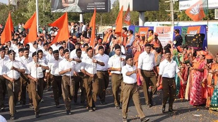 A group of people participating in a Hindu cultural parade holding flags and dressed in traditional.