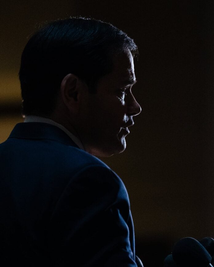 Profile of Marco Rubio in a dark setting, highlighting his facial features.