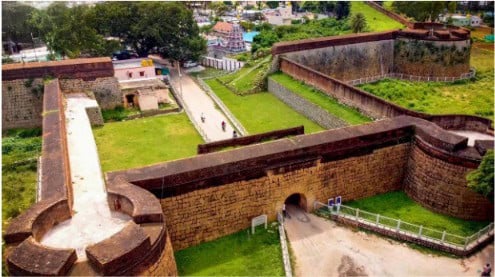 Ancient fort walls and entrance in Devanahalli with lush greenery and pathways.