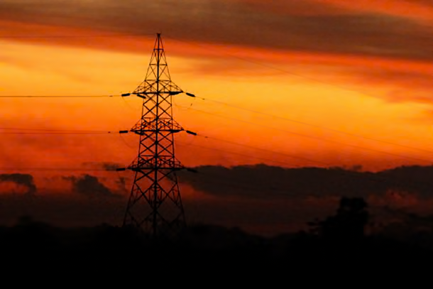 Electricity transmission tower silhouette against vibrant sunset sky.